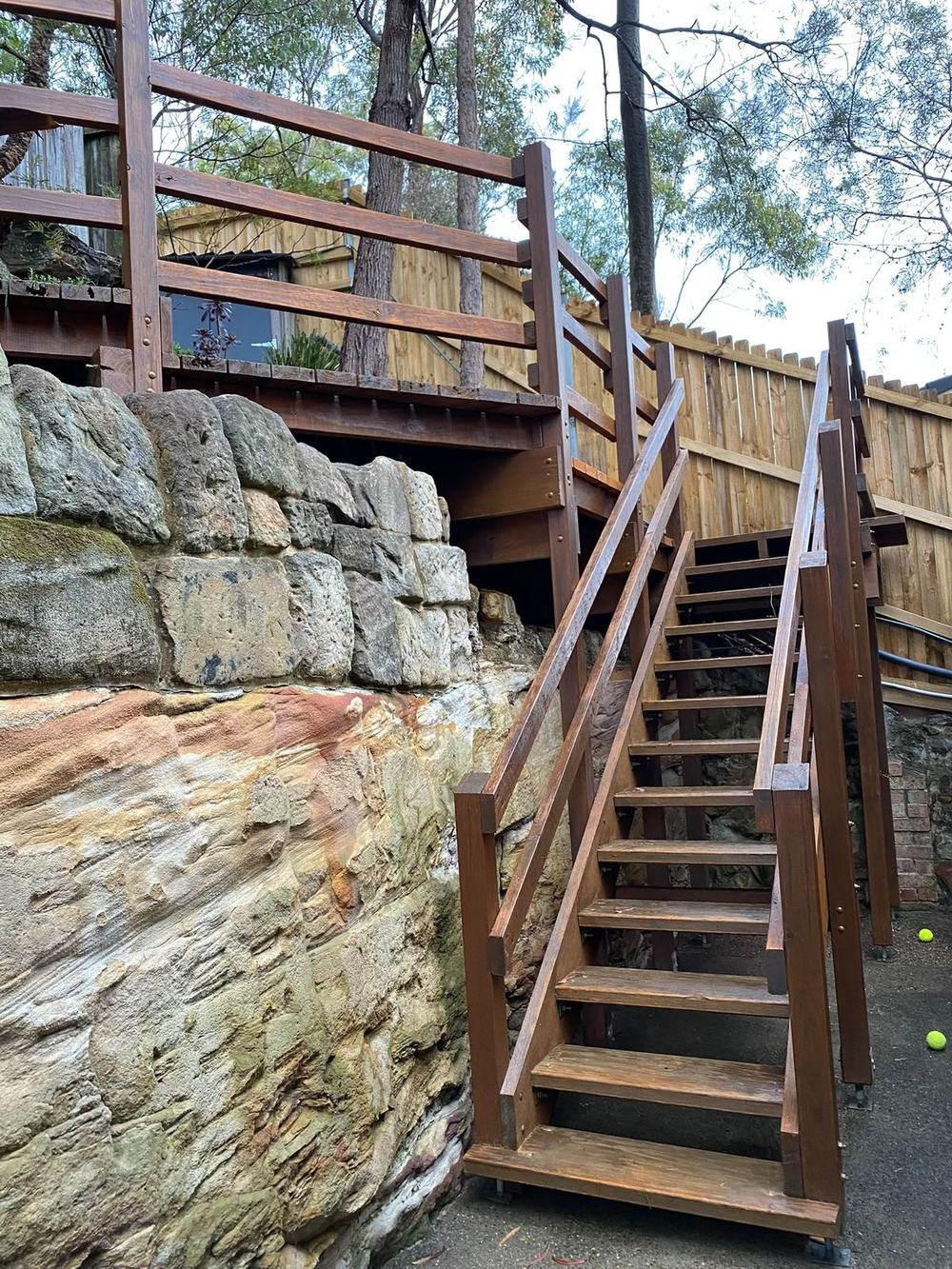 Lower flight of timber garden stairs running down beside a sandstone cliff to a paved base