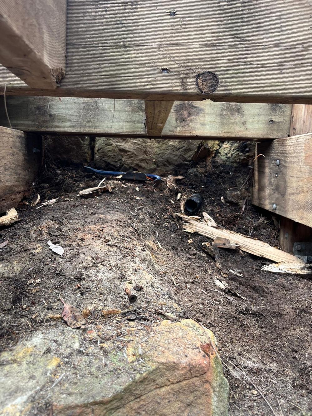 Broken, splintered pieces of rotten timber lying on damp soil under the stairs