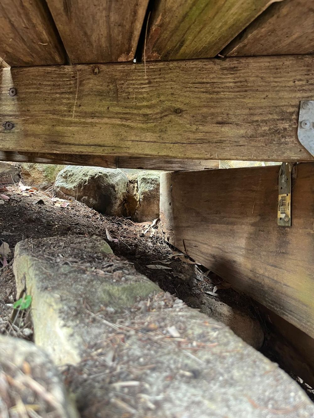 Under the deck, a timber bearer resting right down in soil and gum leaves against a sandstone wall