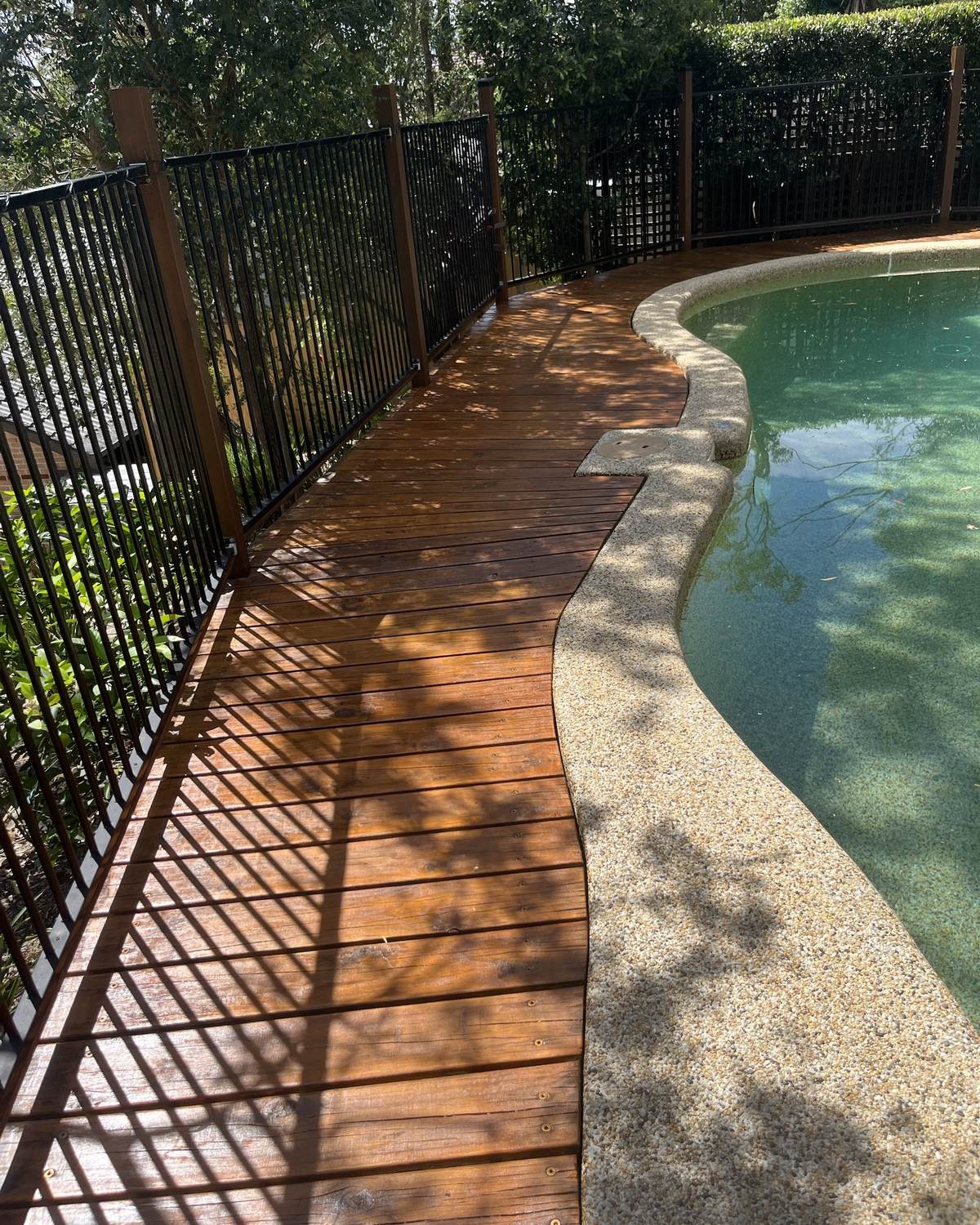 The same pool deck along the fence after sanding and restaining, right up to the pool edge